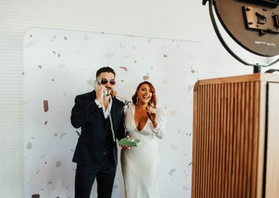 bride and groom with cigar and phone at photobooth